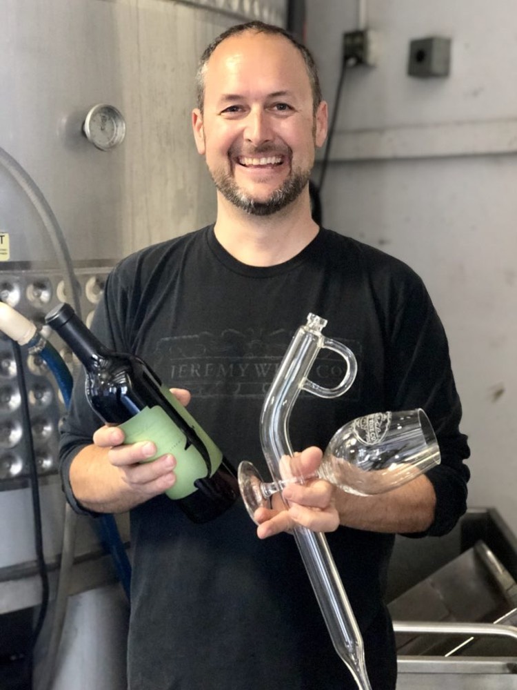 Jeremy in the cellar holding a wine thief and a sample bottle