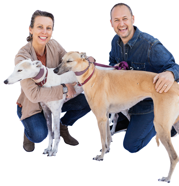 Choral and Jeremy smiling, kneeling beside their two greyhounds