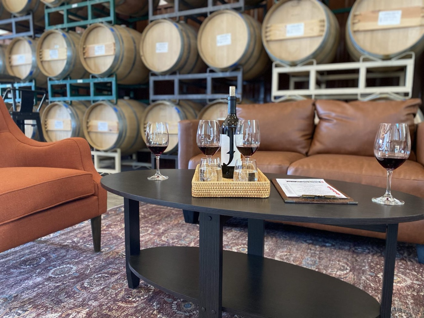 Lounge seating with glasses of red wine in front of stacked barrels